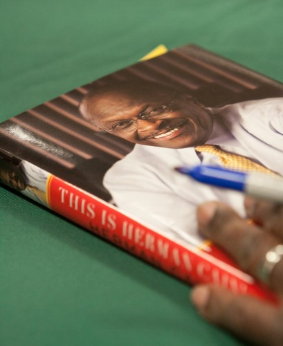 A copy of "This is Herman Cain!" is shown as Herman Cain prepares to sign it.
