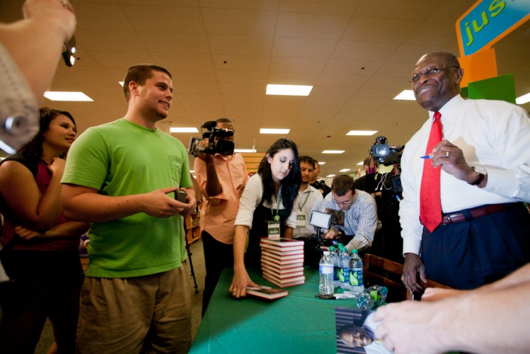 Herman Cain stands behind a book signing table and talks to fans at his book-signing.